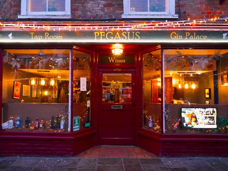 View of the Pegasus from the street, in evening light - the words "tap room" and "gin palace" are backlit