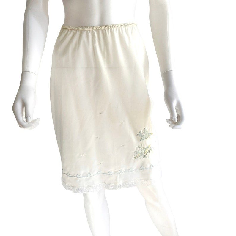 May include: A white slip skirt with a delicate lace trim and embroidered floral details.