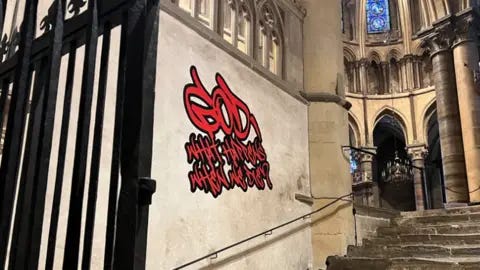 Canterbury Cathedral Red graffiti-style writing is on an ancient stone church wall. 