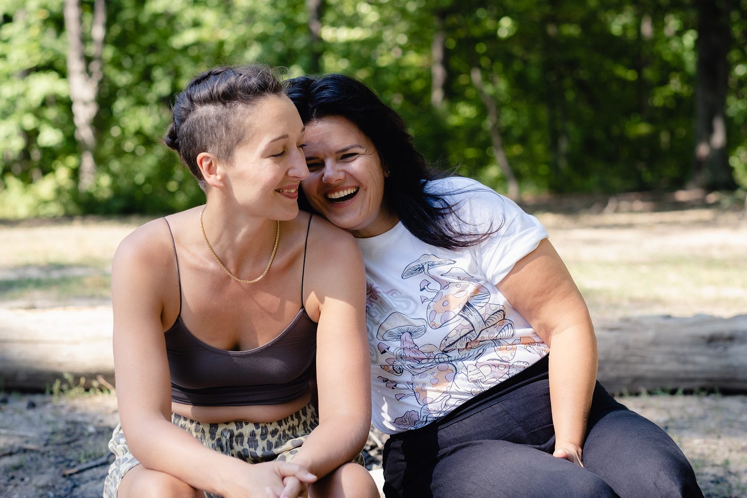 Tarzan sits on top a picnic bench with her feet on the seat, next to her bestie Kathleen who is smiling widely and resting her head in the crook of Tarzan’s neck