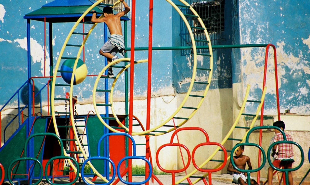 a vintage photo of a child playing on a yellow spiral playground structure with rungs, with two children watching them on the ground