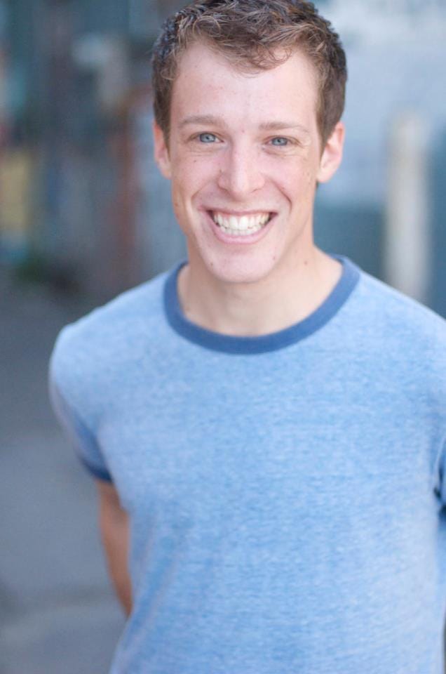 mickey rowe smiles into the camera wearing a blue shirt