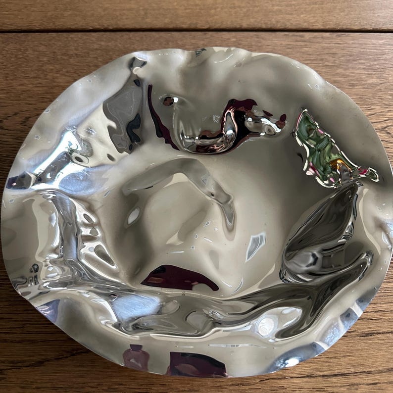 May include: A silver metal bowl with a wavy, rippled surface. The bowl is empty and has a reflective surface.