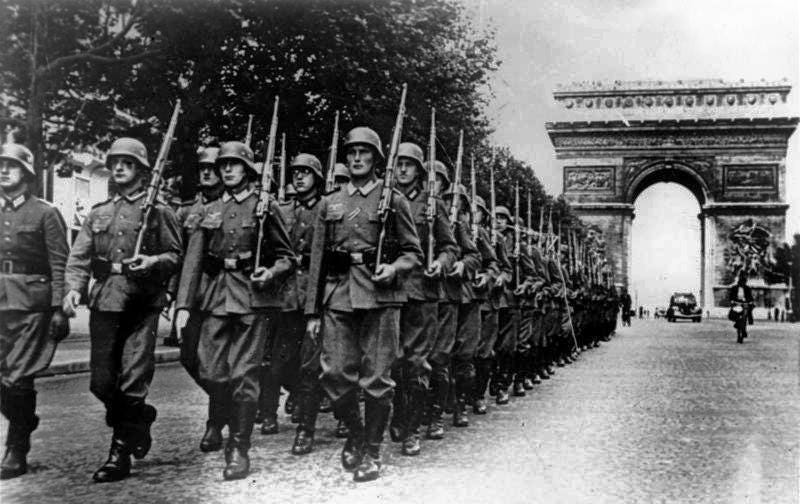 WWII German troops marching with rifles, the Arc de Triomphe in the background. Black and white image.