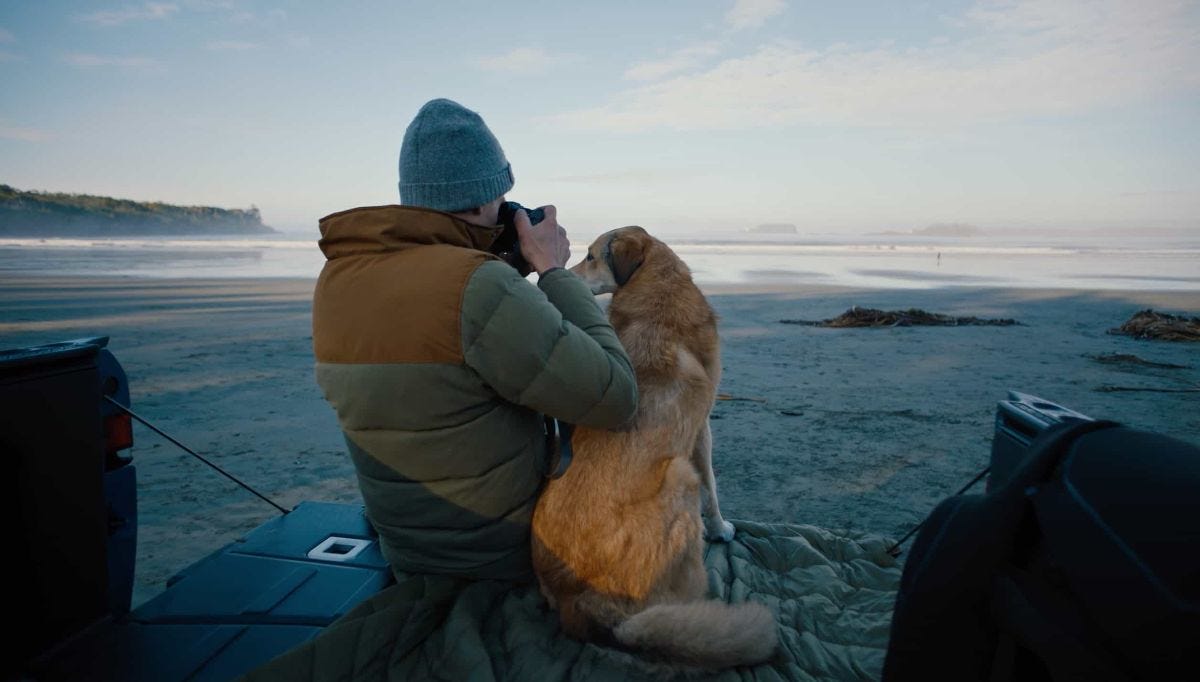 ben moon shoots a photo of the ocean from the bed of a truck with his dog by his side