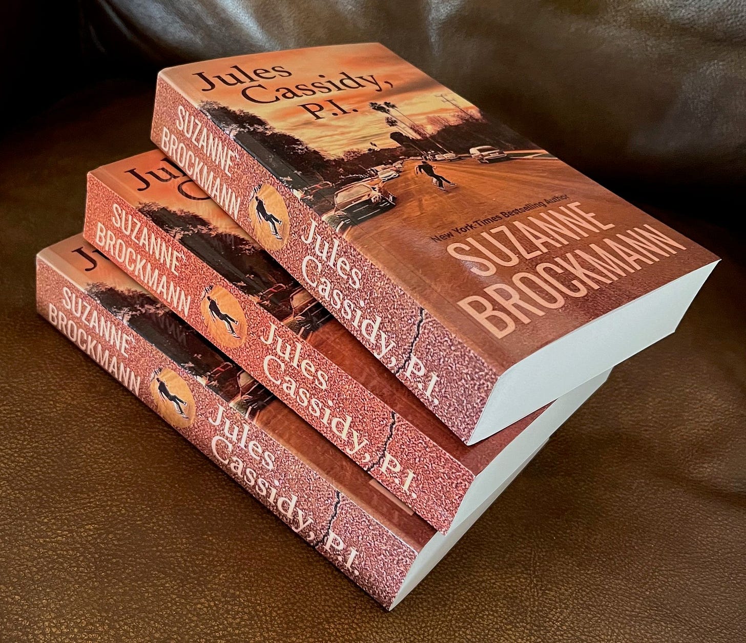 Three paperback copies of Jules Cassidy, P.I. by Suzanne Brockmann are stacked haphazardly on the seat of a leather chair. Three paperback copies of Jules Cassidy, P.I. by Suzanne Brockmann are stacked haphazardly on the seat of a leather chair.