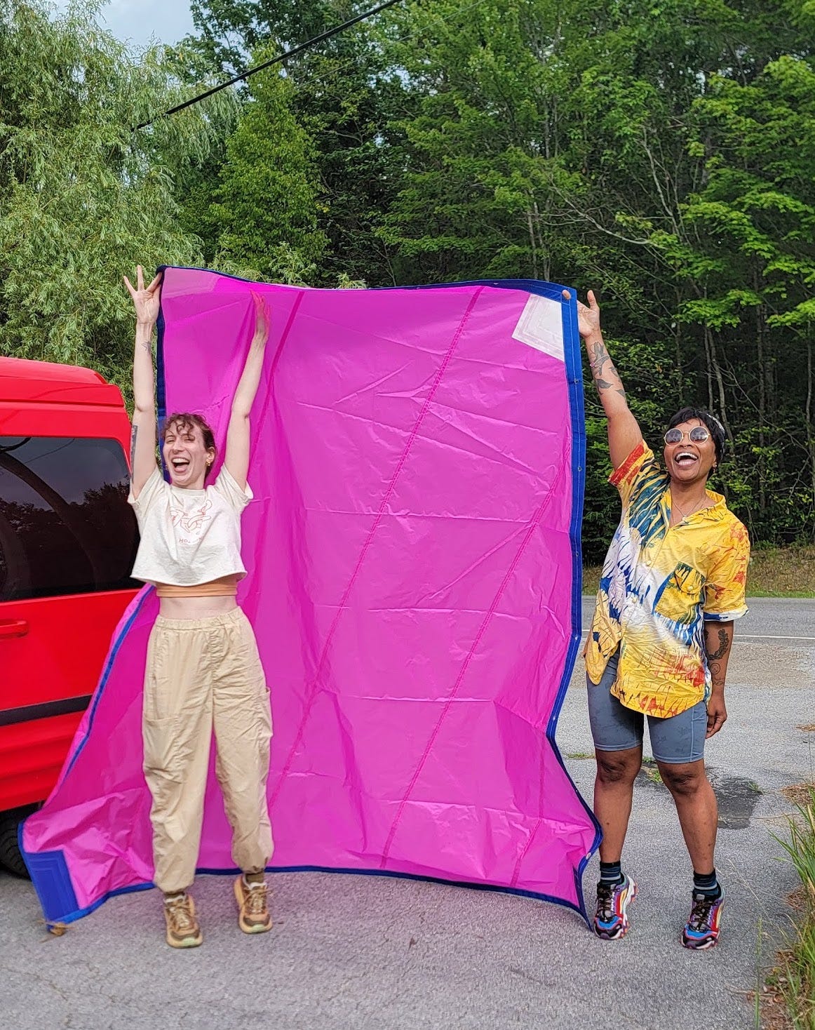 Two artists hold bright pink sail up over their heads grinning.