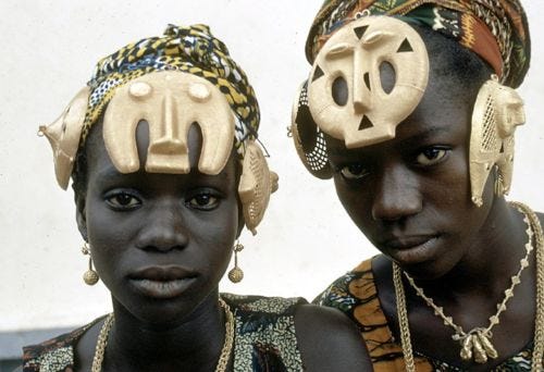 This may contain: two african women wearing head coverings and gold ear rings, both looking at the camera