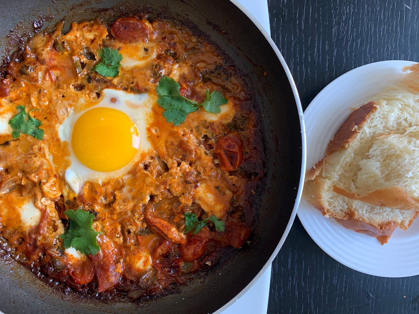 A spicy shakshuka, cooked and photographed by Liat Portal for Foodie Disorder, featuring a perfectly poached egg resting in a bold, deep red tomato sauce with sautéed onions, bell peppers, and melted cheese. Served with soft, buttery brioche on a white plate, this dish represents the rich, layered flavors of shakshuka. Captured for The Liat Show, this photo highlights the depth of Israeli cuisine.