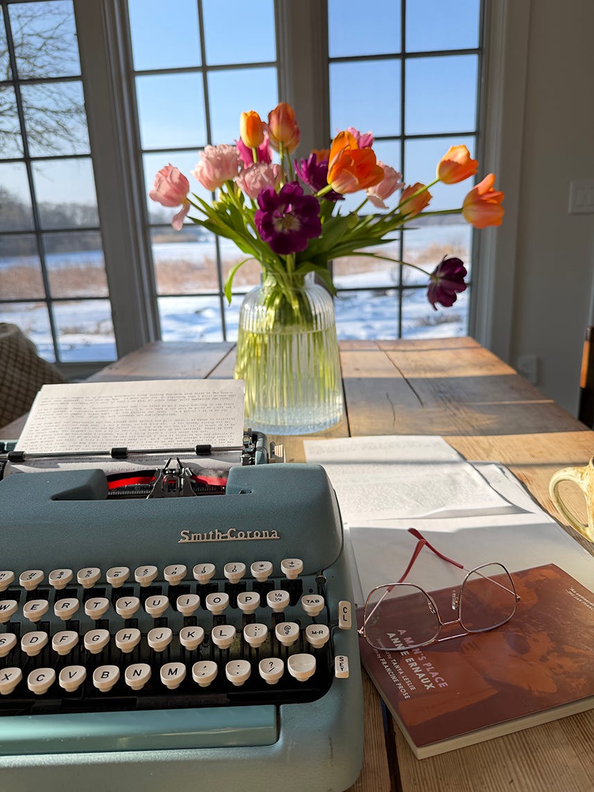 Vintage Smith-Corona typewriter on a desk with flowers and a book in the background