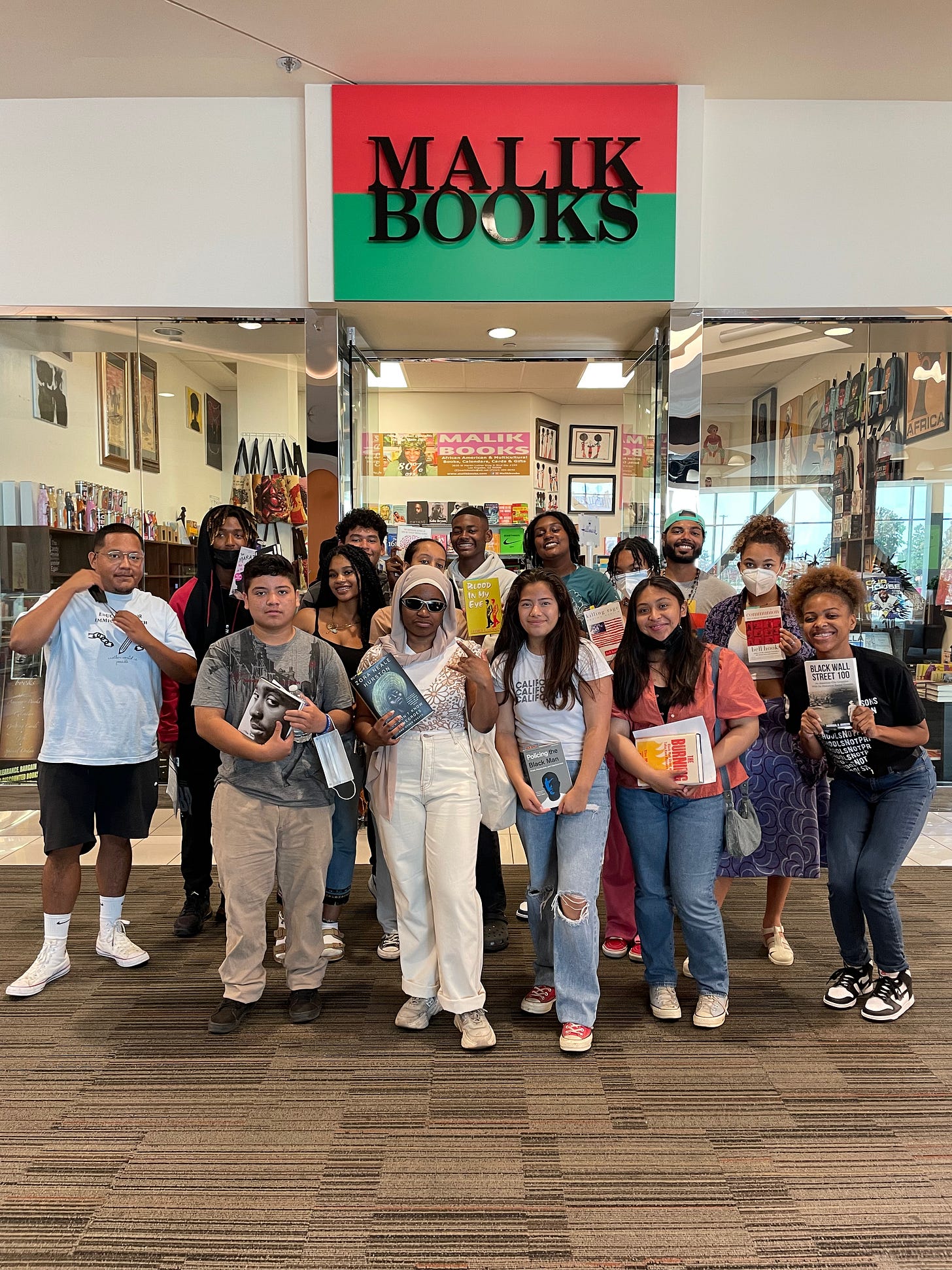 A group of young readers posing with books inside Malik Books A group of young readers posing with books inside Malik Books
