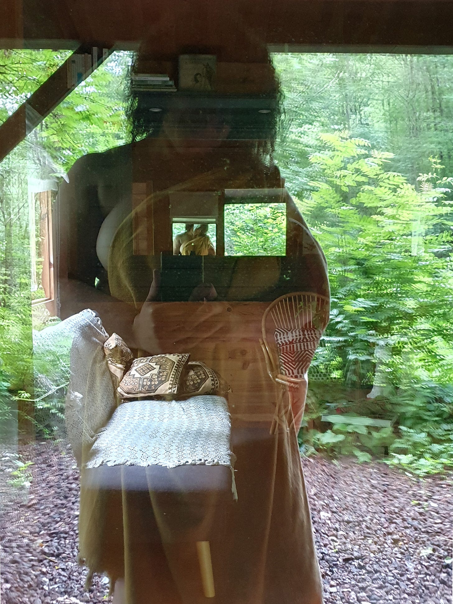 Photo of a woman taken through a window with the furniture in the room showing. She is naked but covered in a throw.
