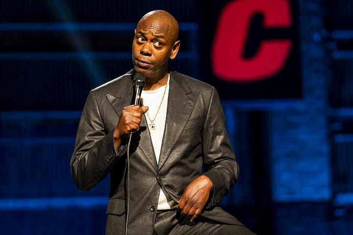 Clockwise from top left: Dave Chappelle onstage with a microphone, trans YouTuber Natalie Wynn, singer-songwriter Azaelia Banks, and trans adults film star and YouTuber Buck Angel