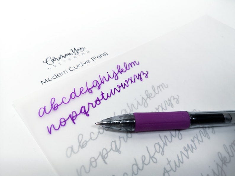 May include: A close-up of a purple pen on a white sheet of paper with the alphabet written in cursive. The text "Carmen Yan Lettering Modern Cursive (Pens)" is visible at the top of the page.
