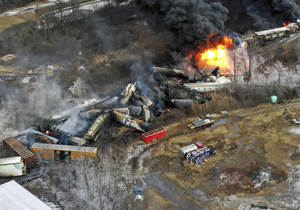 Aerial view of a derailed freight train on fire with black smoke and overturned tank cars. 