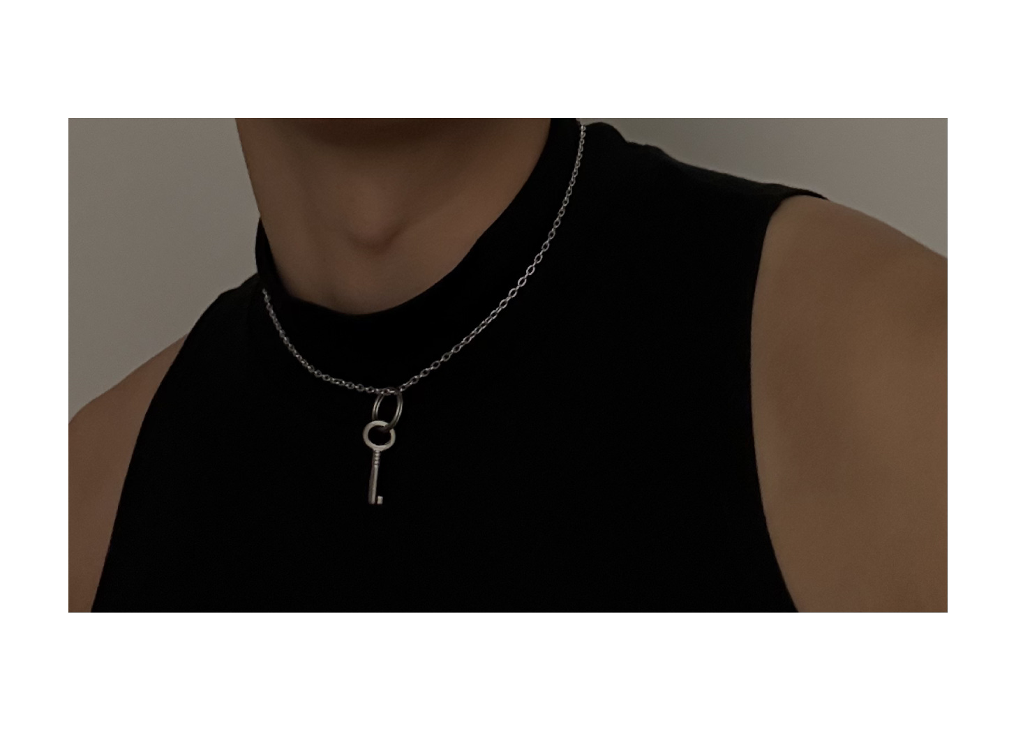 cropped photograph of a person wearing a black sleeveless shirt and a silver chain necklace strung with a singular metal key
