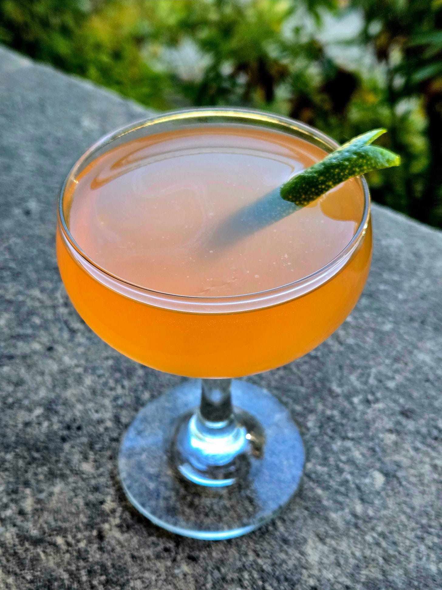 Pegu Club cocktail in a coupe glass with lime twist garnish sitting atop stone.