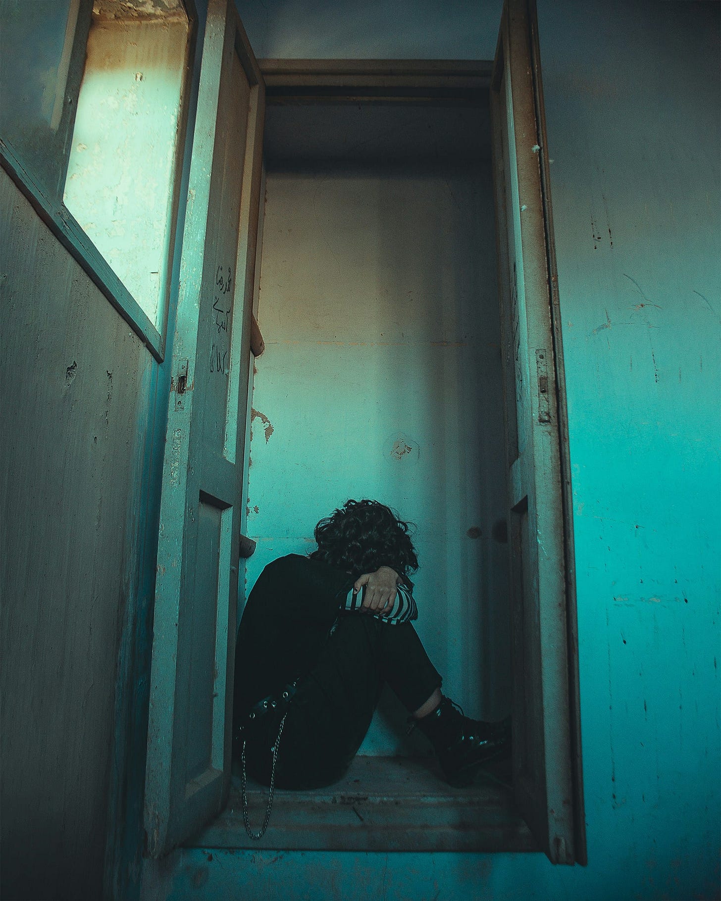 Woman sitting in a cupboard with her knees to chest, arms and head draped over, curled up Woman sitting in a cupboard with her knees to chest, arms and head draped over, curled up
