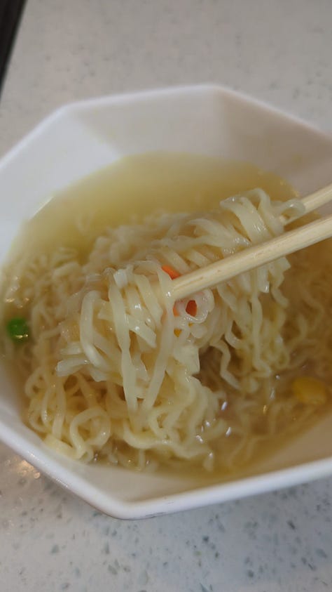 Classic chicken instant ramen cup being opened, cooked, and held up by chopsticks.