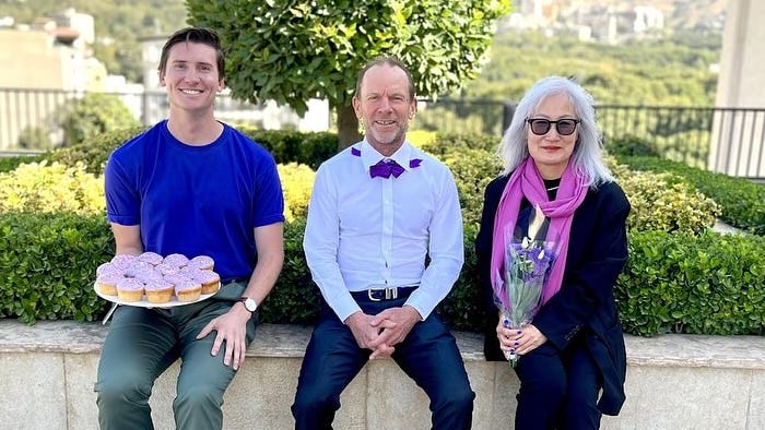 Mad on left holds cupcakes while sitting next to another man and woman Mad on left holds cupcakes while sitting next to another man and woman