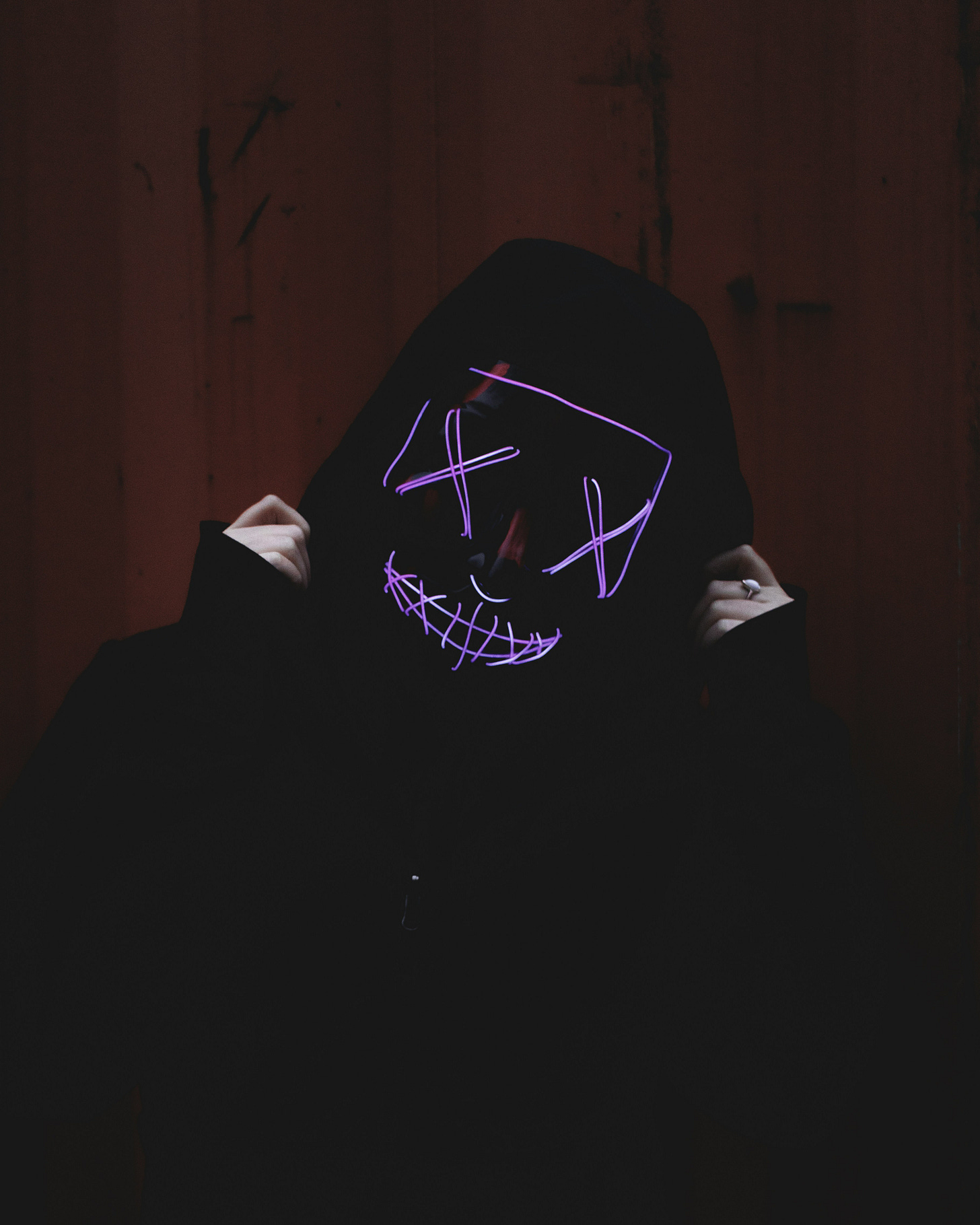 A person wearing a black outfit pulling hood with pinkish-purple X for eyes and teeth.