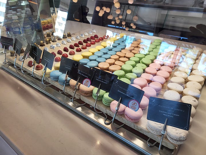 a coastal shore with a light house next to a shelf of macaroons, next too a beach, next a dimly lit walk walkway in the forest