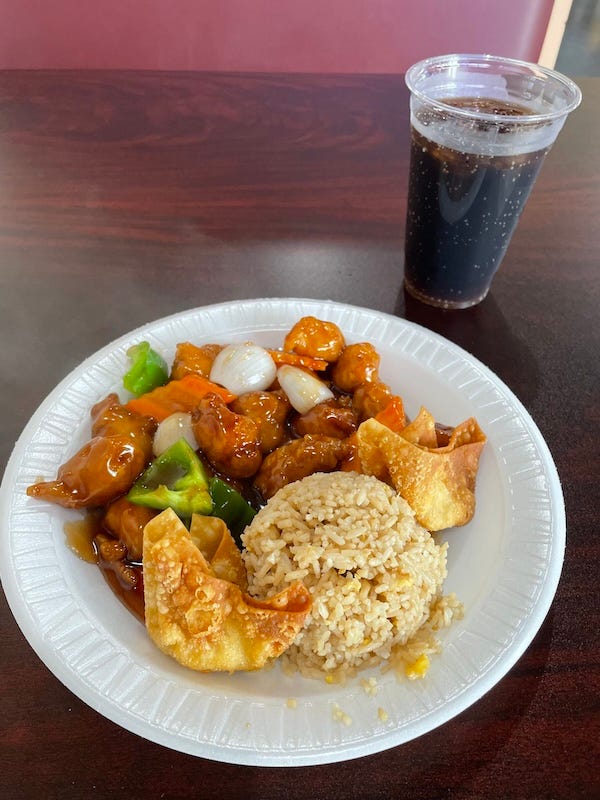 A styrofoam plate with a chicken-and-vegetable entree, fried rice, and two wontons