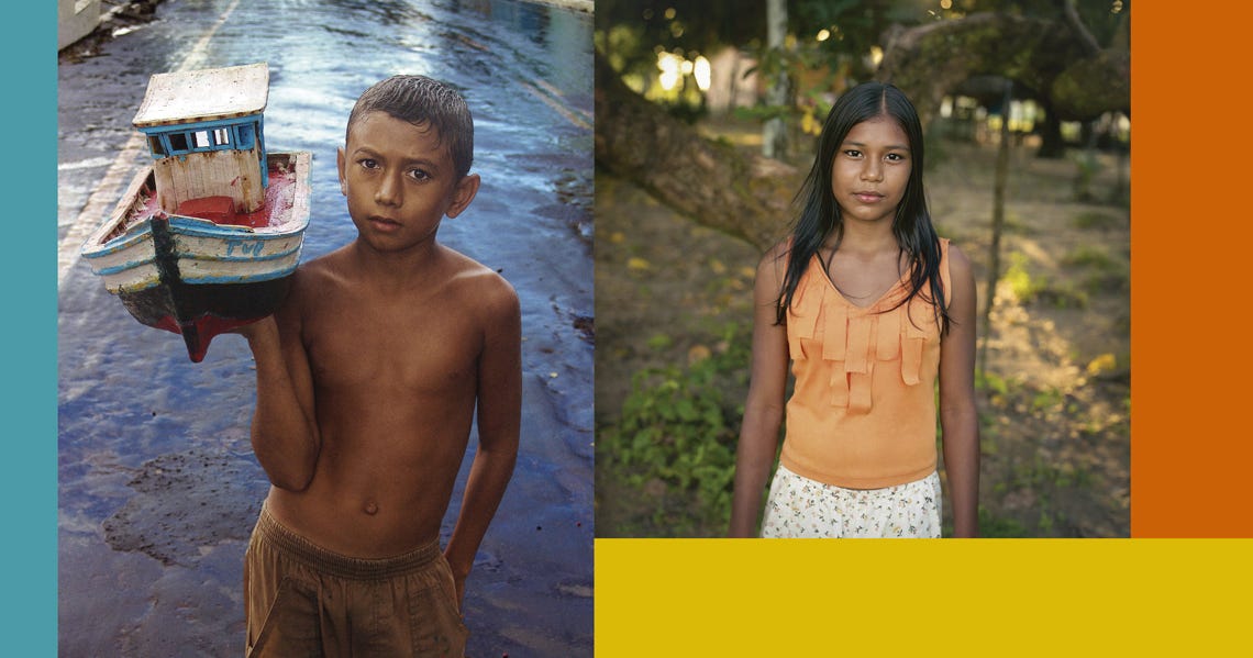 #descrevemospravocê  Imagem dividida ao meio com duas fotografias lado a lado, cada uma destacando o retrato de uma criança em diferentes cenários da região amazônica.  À esquerda, um menino de pele clara e cabelos curtos, molhados, está em pé sobre um chão úmido e irregular, possivelmente de terra batida ou asfalto encharcado. Ele está sem camisa e veste um calção marrom claro. Com uma expressão séria, segura sobre o ombro direito uma pequena réplica de barco de madeira, pintado de azul, branco e vermelho. Ao fundo, vê-se a continuação do caminho molhado e parte de construções desfocadas. A lateral da imagem é emoldurada por uma faixa azul-claro.  À direita, uma menina de cabelos longos e lisos está em pé ao ar livre, em meio a uma área de chão de terra, árvores tortuosas e vegetação esparsa. Ela veste uma blusa laranja sem mangas com babados na parte frontal e uma saia branca com estampa delicada de flores. Olha diretamente para a câmera, com expressão neutra e serena. A cena é iluminada por uma luz suave, provavelmente do entardecer. A imagem é emoldurada por faixas coloridas nas laterais: uma laranja à direita e uma amarela na parte inferior.  A composição evidencia a identidade e o cotidiano de crianças amazônidas em suas paisagens naturais e culturais, valorizando suas histórias por meio de retratos simples, diretos e expressivos.