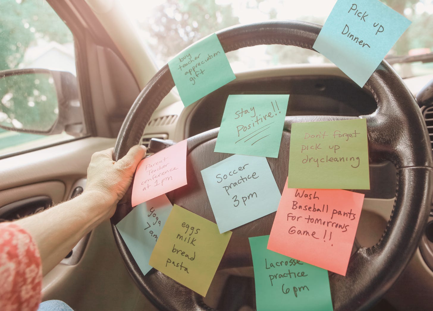 A car steering wheel covered in colorful sticky notes with reminders for errands, appointments, and tasks—symbolizing the mental load and invisible labor parents often carry for their families.