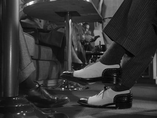 The contrast of Bruno's bolder suit trousers and two-tone shoes communicate that he will be the agent of chaos for the more soberly dressed gentleman with whom he collides on the train.