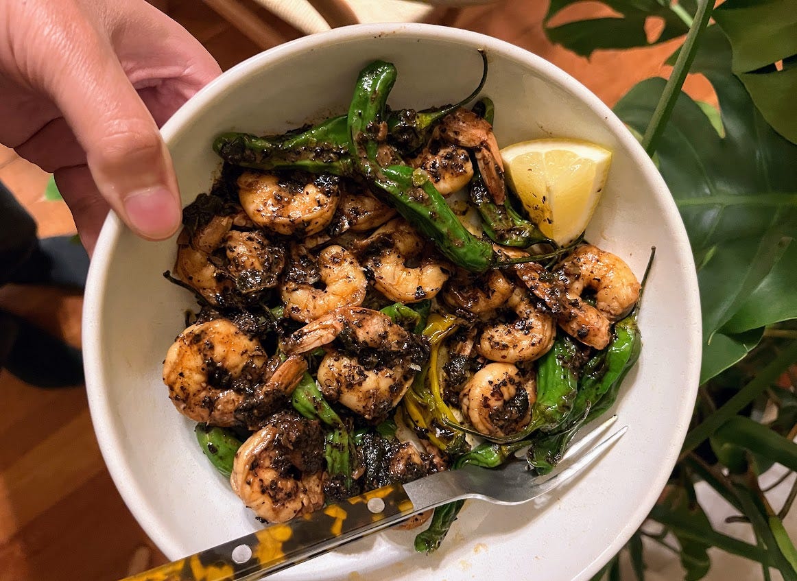 hand holding plate of shishito peppers and shrimp