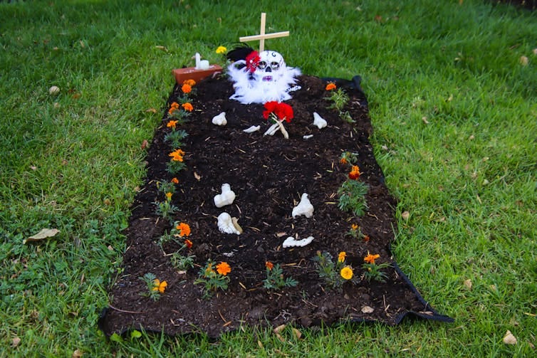 A grave with orange flowers, a cross and a skull on it.