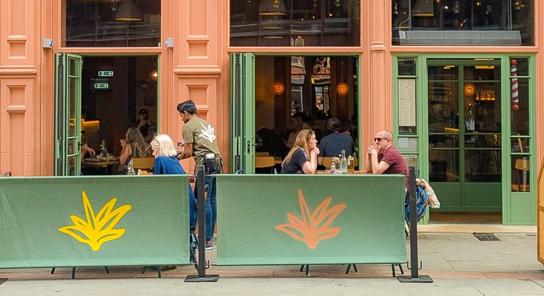 A terracotta building with green doors and signage, with people dining outside A terracotta building with green doors and signage, with people dining outside