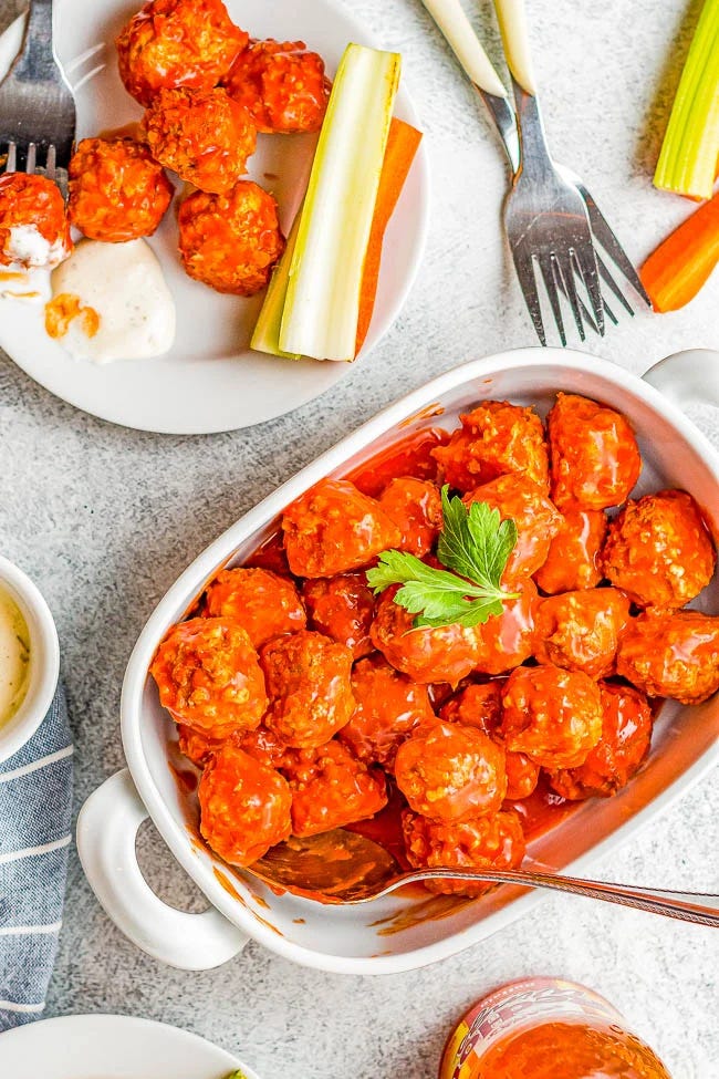 A serving dish of buffalo chicken meatballs garnished with parsley, with celery sticks, dipping sauce, and utensils on the side. A serving dish of buffalo chicken meatballs garnished with parsley, with celery sticks, dipping sauce, and utensils on the side.