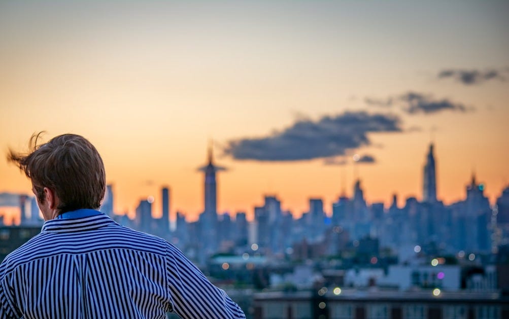 man in blue and white striped shirt looking at city skyline during daytime