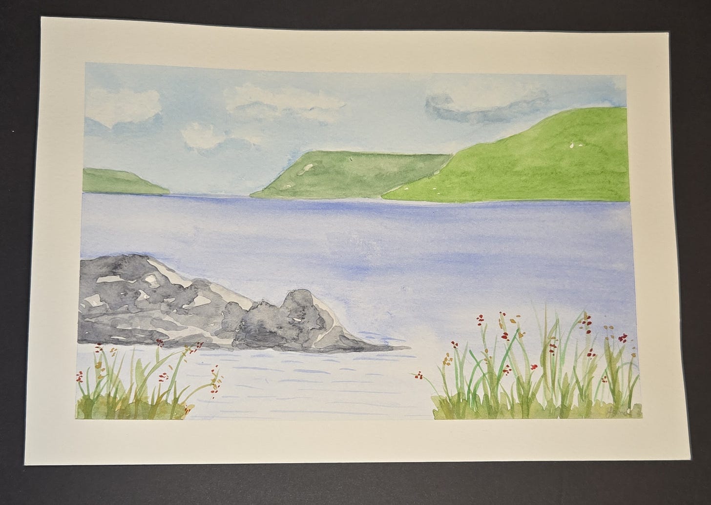 Watercolor landscape of a blue lake bordered by grasses and flowers, with distant green hills under a cloudy sky.