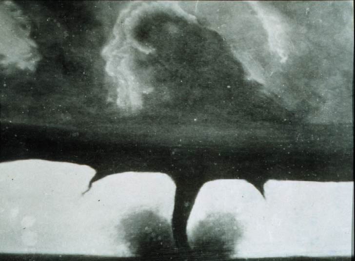 Black and white photograph of a tornado in the center, flanked by a funnel cloud on either side.