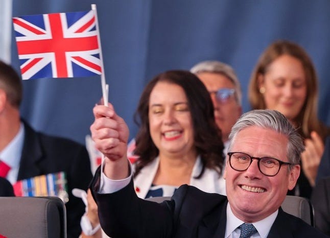 Keir Starmer smiles while waving a Union Jack flag