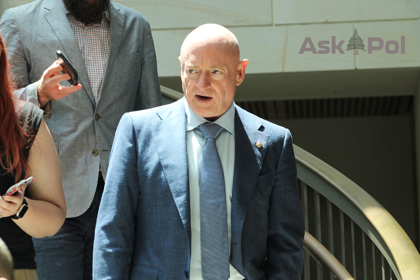 A bald man in a suit walks down a sunny stairwell followed by two others with their phone recorders out. Photo: Logan Johnson © www.askapolpolitics.com 