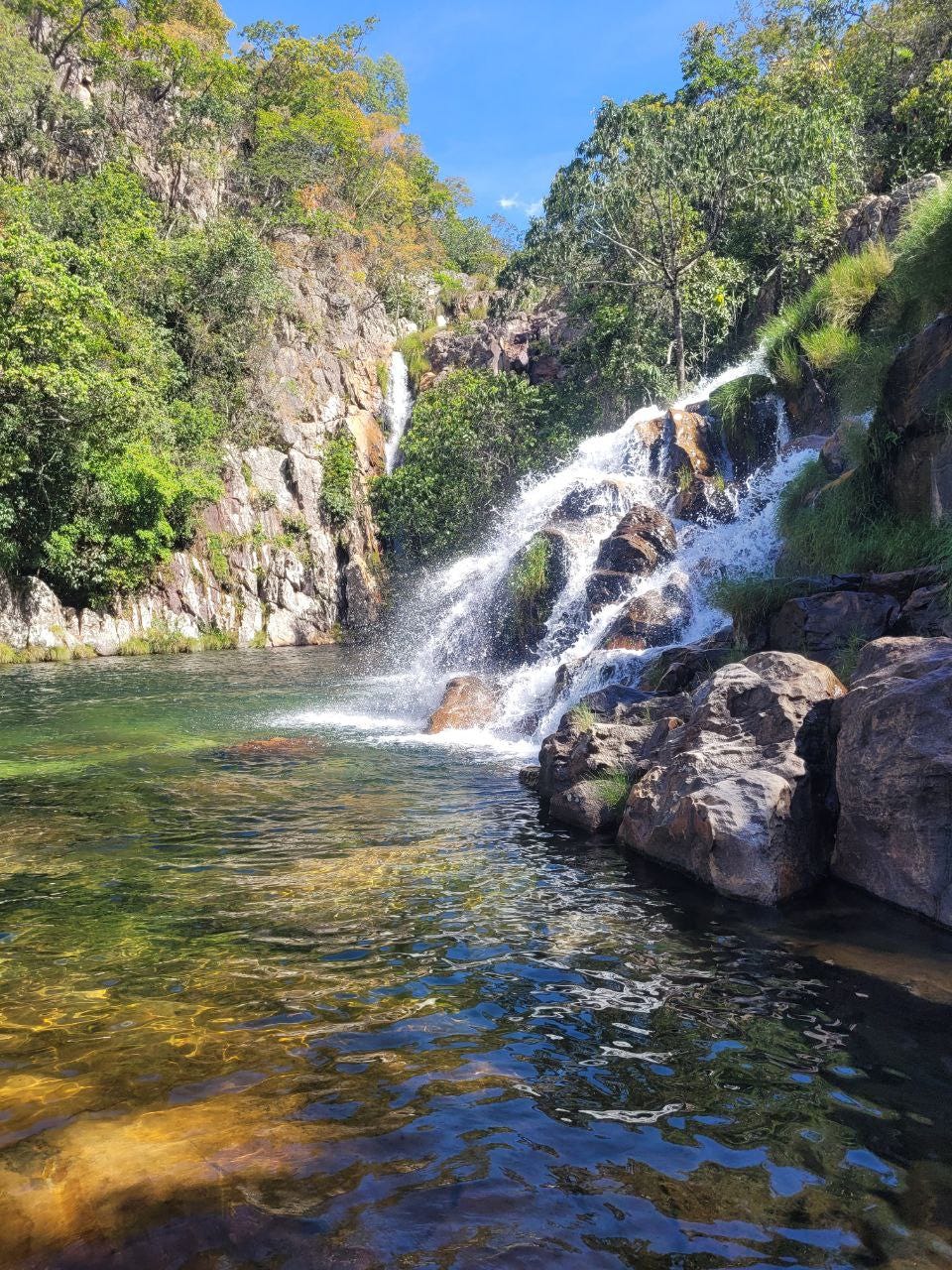 Cachoeira mais espalhada, vista na lateral direita, rodeada de muita natureza, e caindo em um poço esverdeado.