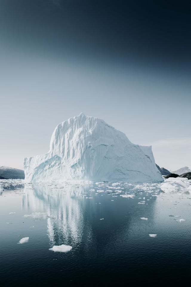 A large iceberg on the top of a expanse of dark water filled with smaller shards of ice and a reflection of the iceberg.
