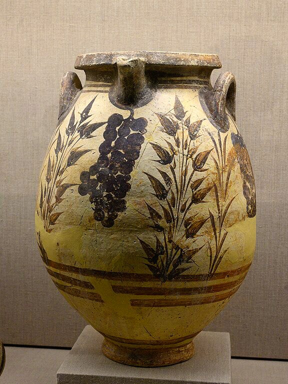 Tall vase with a spout, flared rim, and two looped handles just under the rim. The vase is painted with clusters of grapes hanging from the upper edge. The grapes alternate with clusters of foliage sprouting from the base; the foliage includes sprigs of grass or reed and plants with pointy seed pods.