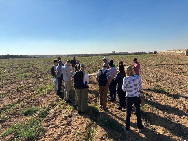 Une dizaine de personnes, debout, l'air concentré ou regardant par terre, au milieu d'un champ de terre brûlée par la sécheresse. Une dizaine de personnes, debout, l'air concentré ou regardant par terre, au milieu d'un champ de terre brûlée par la sécheresse.