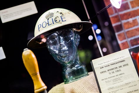 Photographs showing tin hats with 'Police' written on them, bullseye lamps, a hand bell, metal County Police signs and medals.