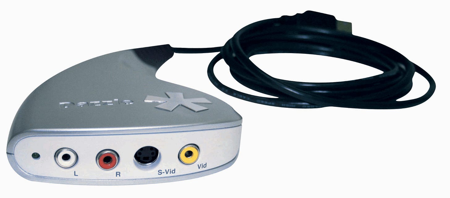 A Dazzle USB video capture device with RCA and S-Video input ports and a USB cable.