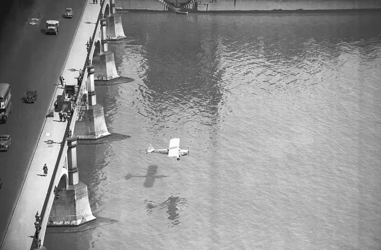 b/w photo of an absurdly small plane emerging on the other side of Westminster Bridge
