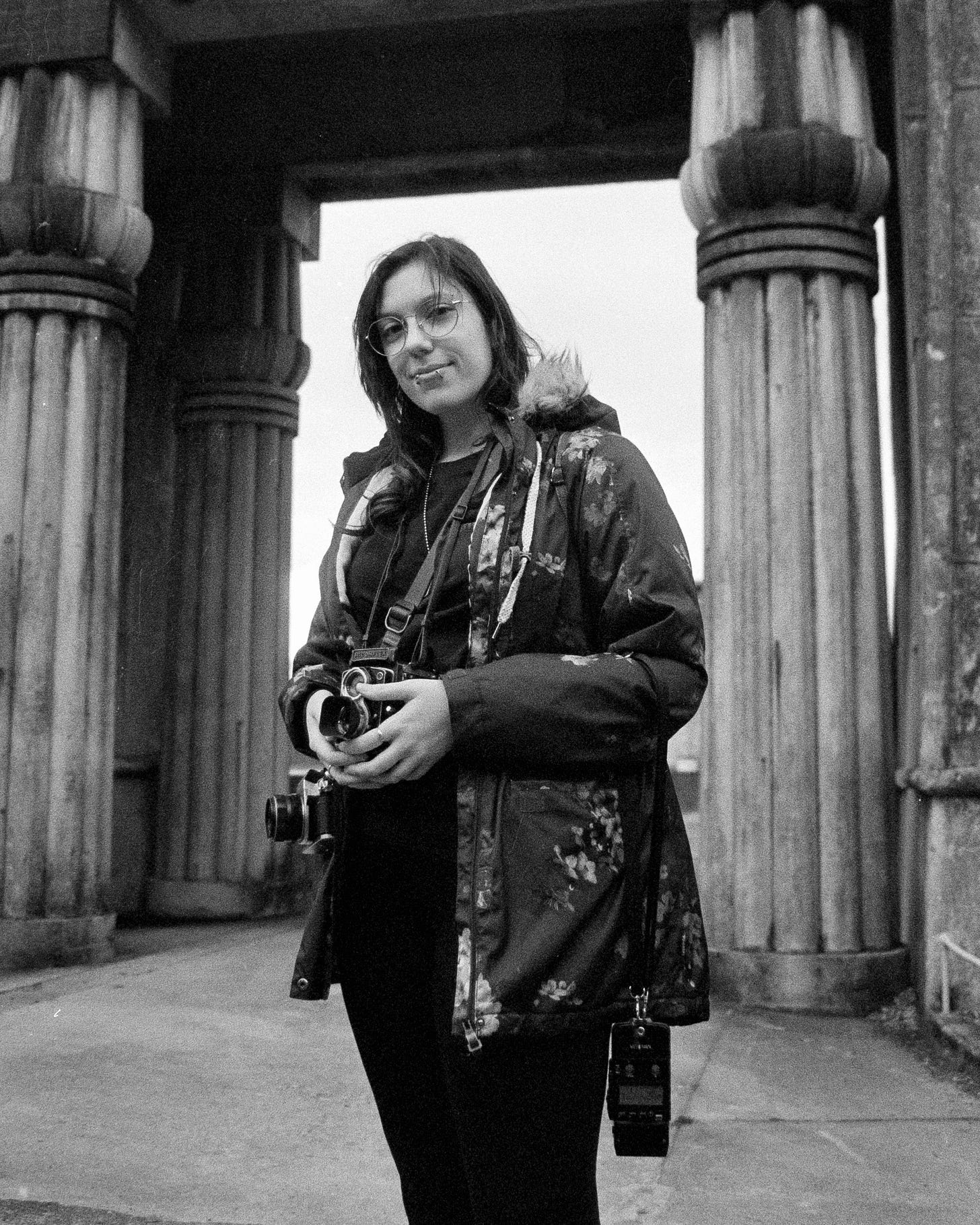 A photo of Josie shot on black and white film, she’s wearing an oversized snow jacket, and holding two cameras as well as various photography equipment. A soft smile on her face as she tests new gear for the first time. A photo of Josie shot on black and white film, she’s wearing an oversized snow jacket, and holding two cameras as well as various photography equipment. A soft smile on her face as she tests new gear for the first time.