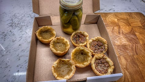 From left to right: a photo of a red shack beside a country road with a sandwich board outside. There's a little window in the side of the shack with a counter. Next, a photo of a man with a large white beard in the shack. There are containers of butter tarts surrounding him. On the counter there is a jar of pickles and a price list. Finally, there is a shot of an open box containing the butter tarts and jar of pickles we bought.