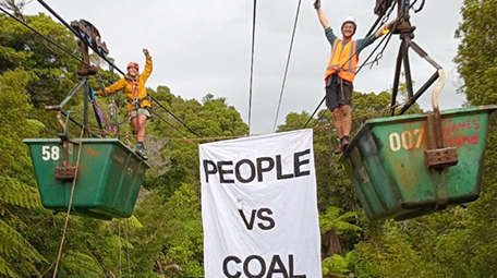 Photo of protesters standing on coal buckets in the air and hanging a banner