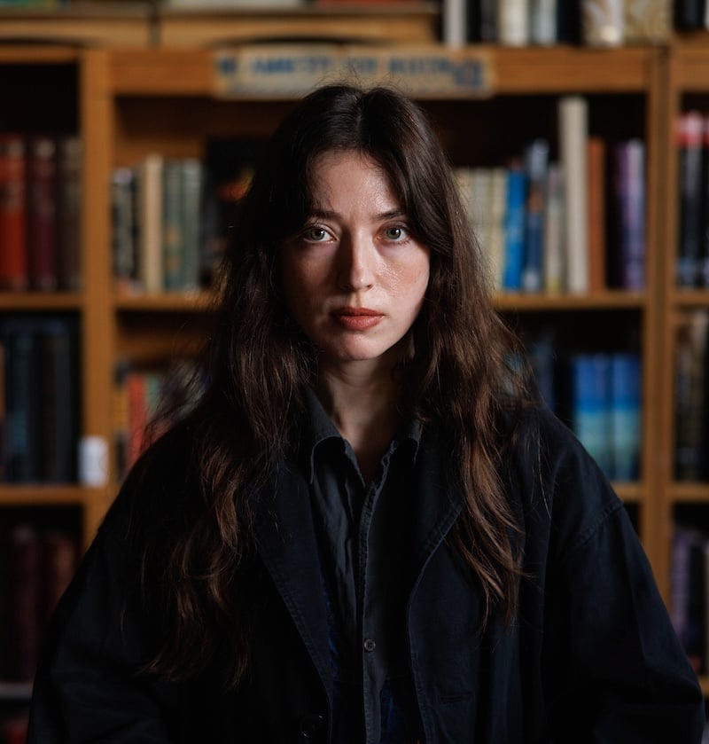 Author Devyn Defoe posing in front of a packed bookshelf